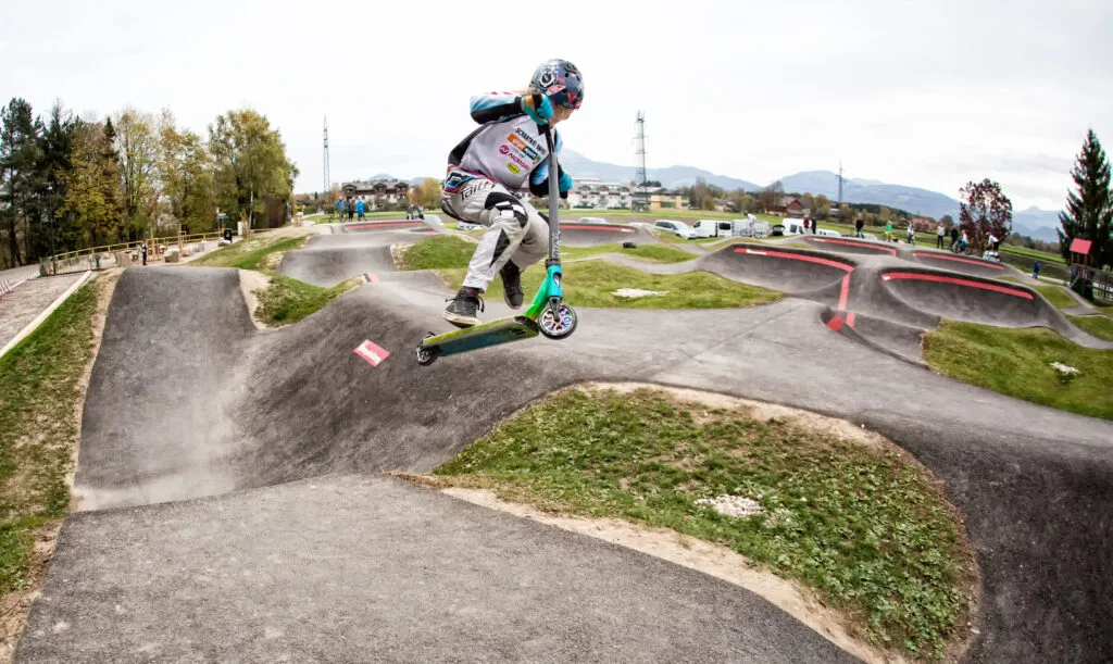 Man sieht ein Kind mit dem Scooter auf einem Pumptrack
